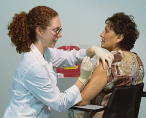 Health care provider preparing to give injection in patient's upper arm.