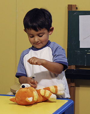 Child playing with pretend syringe and teddy bear.