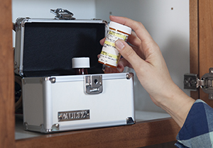 Person putting pill bottle in locking box in cabinet.