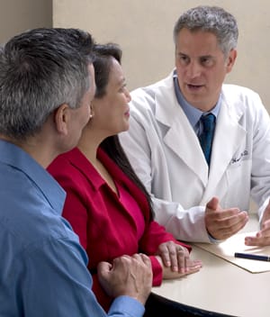 Two people sitting at desk talking to doctor.