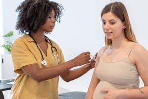 In a doctor’s office, doctor gives a vaccine in the upper arm of a pregnant person.