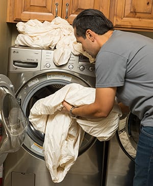 Person loading sheets into home washing machine.