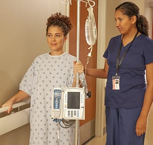 Health care provider walking with patient in hospital hallway.