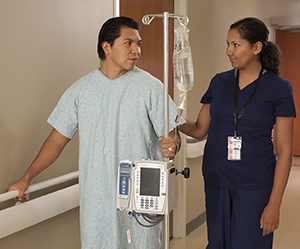 Health care provider walking with patient in hospital hallway.