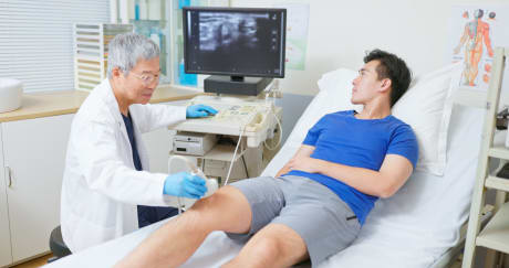 Health care provider placing transducer on person's knee, with images shown on a computer monitor.