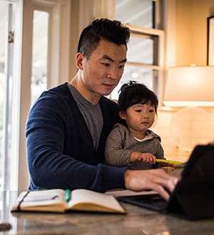 Man holding child and typing on computer.