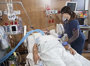 Health care provider caring for intubated patient in intensive care unit.
