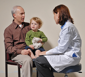 Boy sitting on man's lap while man talks to doctor.