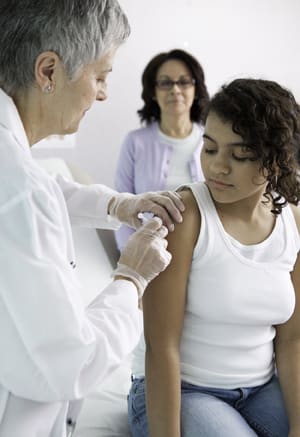 Doctor giving shot in child's upper arm. Woman standing in background. 